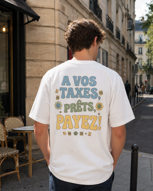 "Photographie lifestyle d'un homme de dos portant le t-shirt blanc 'À VOS TAXES, PRÊTS, PAYEZ !' dans une rue typique avec une terrasse de café en arrière-plan.