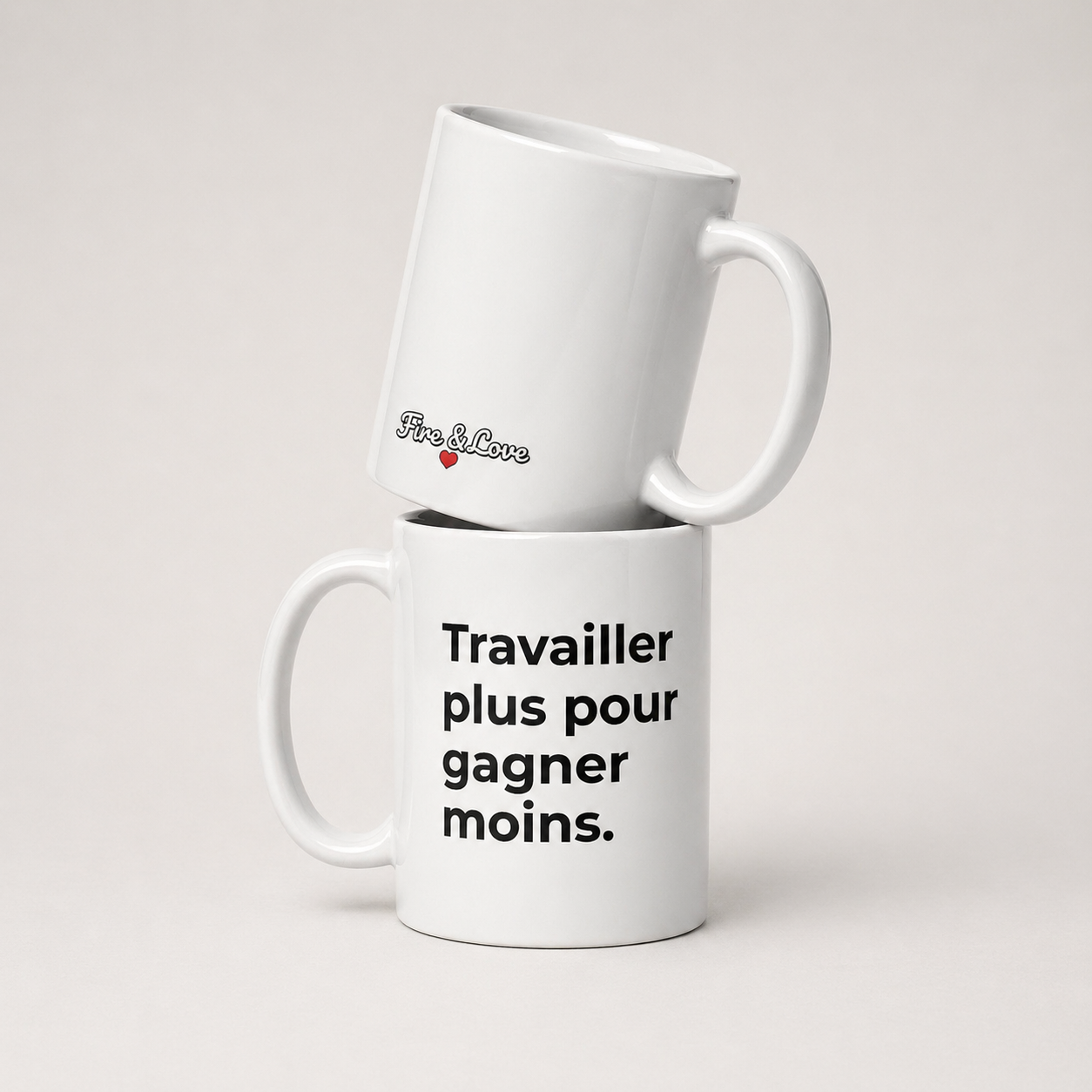 Photographie de deux mugs en céramique blanche empilés sur un fond gris clair. Le mug du bas affiche le texte noir « Travailler plus pour gagner moins. ». Le mug du haut, légèrement incliné, présente le logo « Fisc & Love » écrit dans une police cursive rétro avec un petit cœur rouge. L'ensemble est présenté dans un style épuré et minimaliste avec une lumière douce.