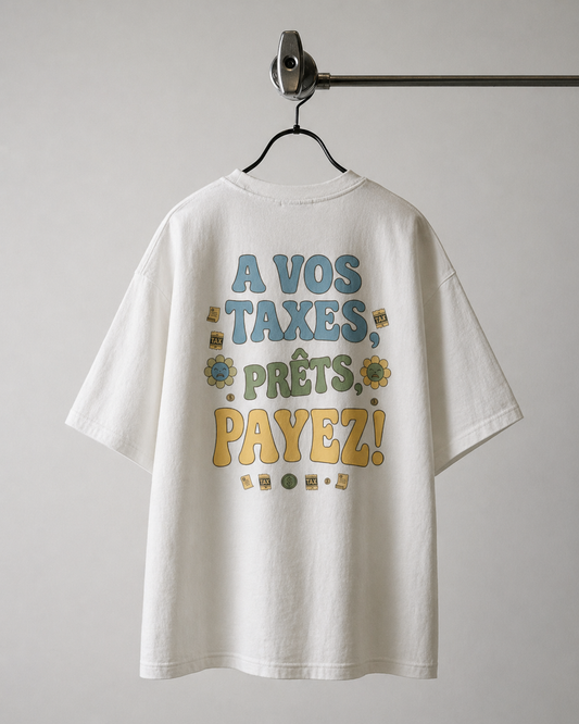 Dos d'un t-shirt blanc oversize avec l'inscription graphique 'À VOS TAXES, PRÊTS, PAYEZ !' en lettres colorées bleues, vertes et jaunes, entourées de petites fleurs et de motifs de formulaires de taxes."