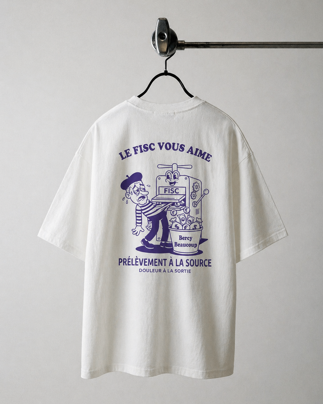"Dos d'un t-shirt blanc oversize sur cintre avec une illustration violette satirique montrant une machine à presser un personnage et les textes 'LE FISC VOUS AIME', 'Bercy Beaucoup' et 'PRÉLÈVEMENT À LA SOURCE'