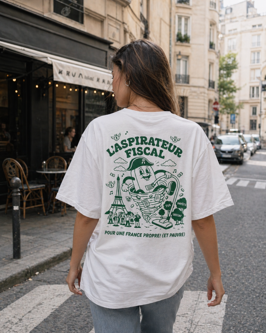 Vue de dos d'une femme marchant sur un passage piéton dans une rue de Paris, portant un t-shirt blanc oversize. Le dos du t-shirt affiche une illustration graphique verte titrée « L'ASPIRATEUR FISCAL ». Le dessin montre un personnage satirique aspirant la Tour Eiffel, de l'argent et des citoyens, avec les mentions « TVA », « IMPÔTS » et « URSSAF ». En bas, on lit le slogan : « POUR UNE FRANCE PROPRE ! (ET PAUVRE) ». L'arrière-plan présente une terrasse de café typique et des immeubles anciens