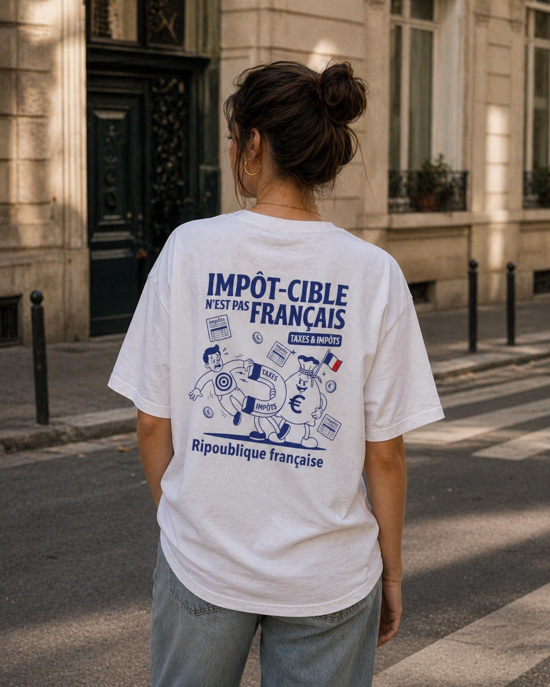 Photo de style de vie prise de dos montrant une femme avec un chignon portant un t-shirt blanc oversize. Le dos du t-shirt affiche une illustration satirique bleue intitulée "IMPÔT-CIBLE N'EST PAS FRANÇAIS". Le dessin montre un personnage en forme de sac d'argent utilisant un aimant pour attirer un citoyen. Elle se tient dans une rue ensoleillée aux bâtiments classiques.