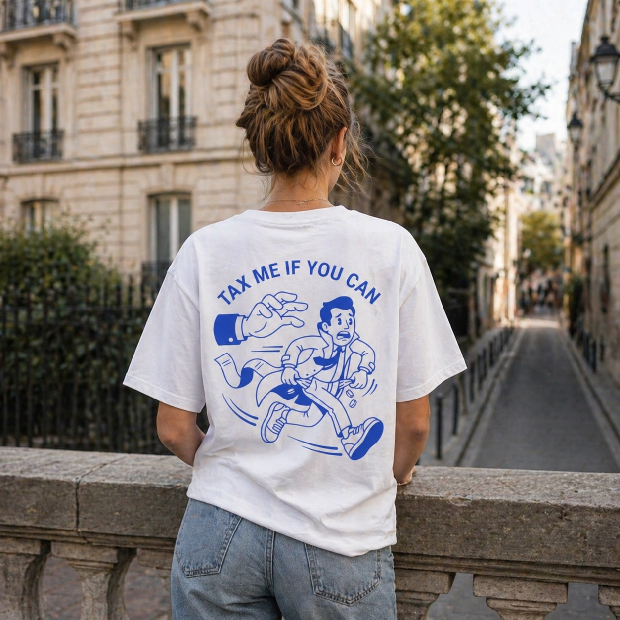 Vue de dos d'une femme avec un chignon haut, accoudée à un pont en pierre surplombant une rue parisienne. Elle porte un t-shirt blanc avec une illustration graphique bleue intitulée « TAX ME IF YOU CAN ». Le dessin montre un personnage en costume fuyant une main géante qui tente de le rattraper, avec des pièces de monnaie tombant de ses poches. Elle porte également un jean bleu clair. L'arrière-plan montre une perspective de rue avec des immeubles haussmanniens classiques.