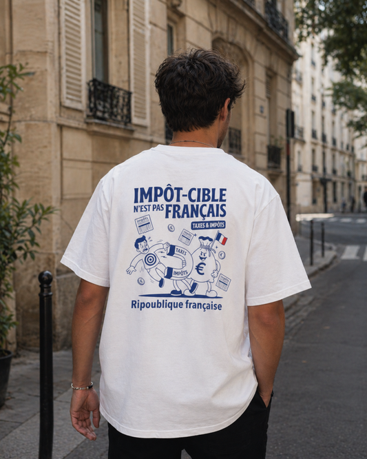 Photo de style de vie prise de dos montrant un homme marchant dans une rue de Paris. Il porte un t-shirt blanc oversize avec l'illustration satirique "IMPÔT-CIBLE N'EST PAS FRANÇAIS". Le graphisme détaillé montre un sac d'argent anthropomorphe "Ripoublique française" utilisant un aimant "TAXES & IMPÔTS" pour attirer un citoyen marqué d'une cible. L'arrière-plan montre des bâtiments haussmanniens flous et une plante en pot
